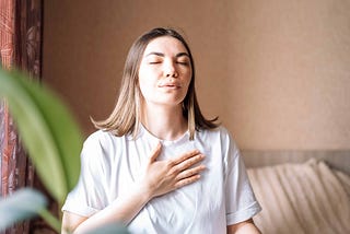 Woman sitting with her eyes closed, focusing on her breathing, with her hand on her chest.