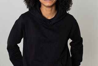 A 20-something black women, with shoulder-length hair, wearing a black sweatshirt, smiling broadly and happily at the camera