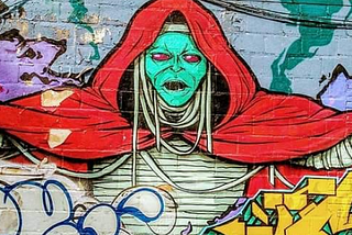 Wall art, graffiti, one painting depicts Mum-Rah, the villain from the cartoon Thunder Cats, arms outstretched, a red cape and white bandages wrapped around arms an torso, evil red eyes glaring