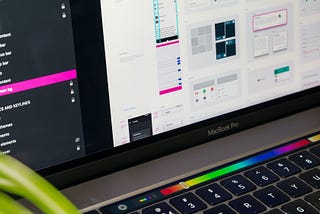 A Macbook Pro with illuminated touchbar, showing design software on the screen