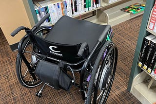 A purple and black wheelchair rounding a very tight corner in a library.