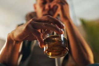 Man holding a glass of alcohol with one hand to his face