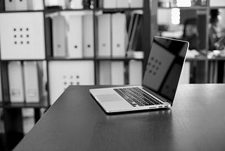Laptop on a table. In the background shelfs.