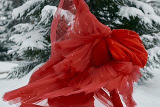 A figure skater wearing flowing red dress and spinning on the ice outdoors.