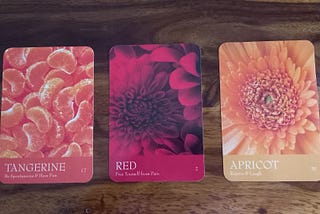 There are three cards from the Secret language of Color Oracle deck; Tangerine, Red and Apricot with pictures of the fruit in the first one, a red dahlia in the second one and an orange dahlia in the third. Choose a pile instinctively.
