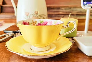 Scalloped and gilded-edge yellow bone China teacup with pink cabbage roses and green leaves painted on the inside of the cup. It sits in its matching yellow saucer and holds golden chamomile tea.