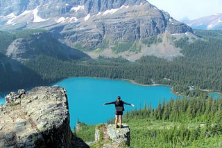Jenna stands on a jutting rock overlooking Lake O’Hara in Yoho National Park. Her arms are outstretched as she takes it in.