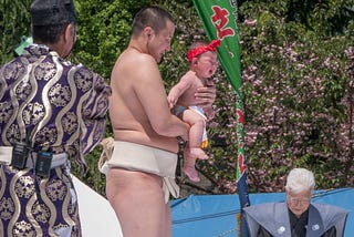 Sumo wrestler holding crying baby at Annual Nakizumo or Crying Baby Sumo Festival in Tokyo, Japan