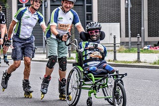 Three men, two rollerblading and one in a wheelchair, are participating in a race.