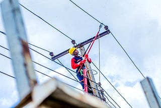 A line worker standing on a ladder does maintenance on a transmission line.