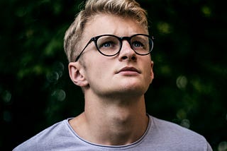 Man wearing black framed glasses looking upwards