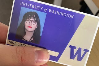 A picture of a University of Washington student ID that says “Nina Lutz” and a picture of the author. The author is a dark haired white woman with bangs, glasses, and red lipstick.