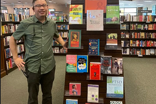 Martin standing beside a bookshelf. He is wearing a green top and black bottoms. Credit: M.Tran