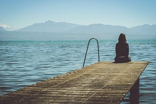 Woman sitting on the edge of a dock looking at the water