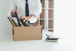 man in a dress shirt and tie packing a box in an empty office