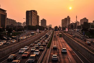 Car traffic on a busy highway with a city skyline and sunset in the background