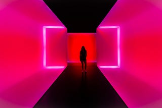 Woman standing in a pink neon-walled room with black floors and ceiling