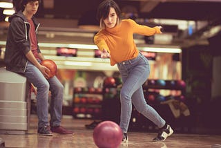 A young woman throwing a bowling ball down the lane, while her date watches.