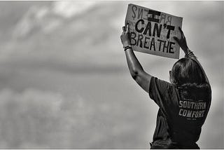 A woman holds up a sign reading ‘I can’t breathe’