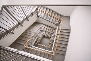 Overhead view looking down a modern interior stairwell with clean lines, neutral tones, and evenly spaced landings.