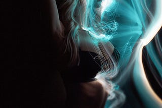 Image of a girl with hands raised above her head, she wears black bra and lace edged underwear. Special effect of swirls of turqouise light are layered onto the image