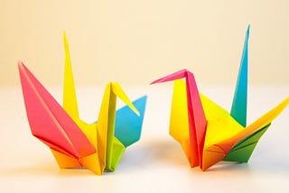 Two multicolored folded paper cranes facing each other.