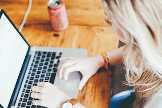 Woman at a laptop with a can of soda nearby.