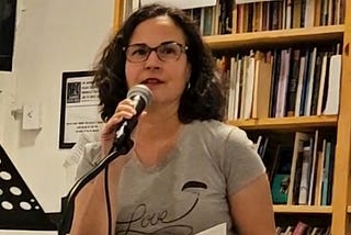 Photo of author at a mic, bookshelves in background