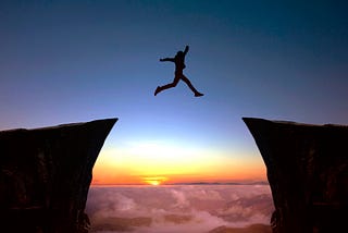 Cool photo of a person’s shadow suspended in air from jumping across a deep chasm. This picture is set against the background of a sunset. The person has both their arms and legs extended while jumping. Picture taken from iStock Photo by gece33. #childfree