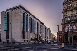 The University of Leeds School of Chemical Engineering Building at sunset, with pedestrians crossing the street next to The Library pub.