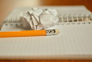 A spiral bound book of graph paper sits open with a crumpled piece of paper and a chewed pencil lying on top.