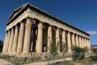 A well‑preserved ancient Greek temple with tall Doric columns stands in an open archaeological site, surrounded by small trees and a gravel path.