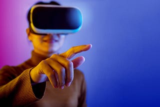 Color photo of an older woman wearing a VR headset and pointing toward the reader.