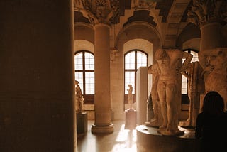 A woman, alone in a museum, looks at several statues.