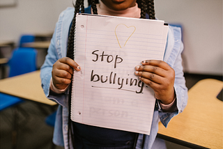 A child’s hands holding up a lined paper notebook that says “Stop bullying”