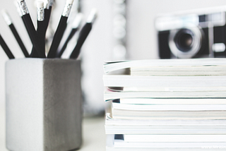 black and white photo of pencils, camera, and stack of books — Human Article Spinner