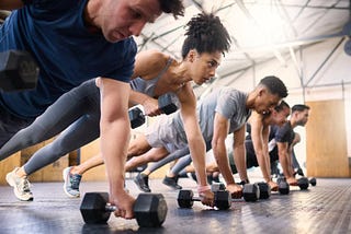 A diverse group of people dressed in fitness attire hold a plank position and do rows with dumbbells