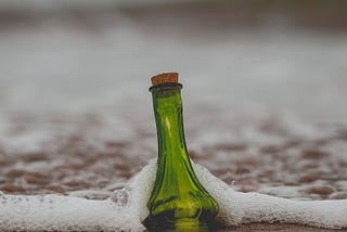 A green bottle surrounded by sea foam on a beach
