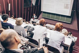A lecture theatre with people sat in the audience and a presenter speaking.