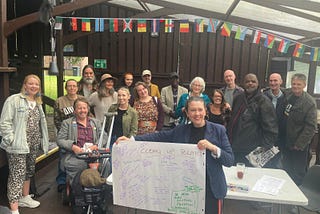 A group of people smile at the camera, a woman at the front holds a piece of paper with ‘Clean Up Politics’ on it