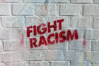 The words: FIGHT RACISM, in all capital, red letters on a white brick wall.