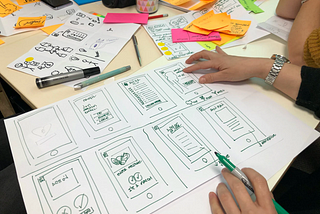 A person drawing mobile screens with different visual ideas on a table surrounded by different colours post-it notes