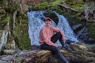 Sophie sat on a tree log in front of Stock Ghyll Force Waterfall