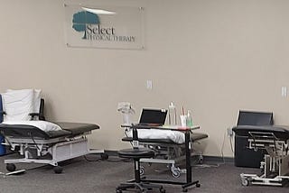 Interior view of a physical therapy office, showing therapy tables, pillows, and a wedge.