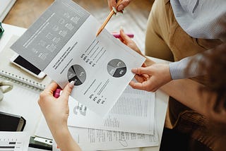 Two people standing and pointing at the summary of an account, along with data visualizations and other numbers