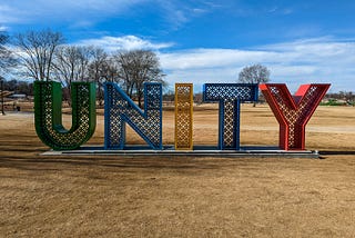 Large metal sign in a field reading U N I T Y