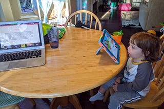 Child looking at ipad while adult computer is open