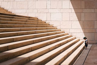 A child waiting at the bottom of very wide steps, getting ready to take the first step.