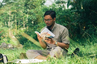 Young man reading book near river.