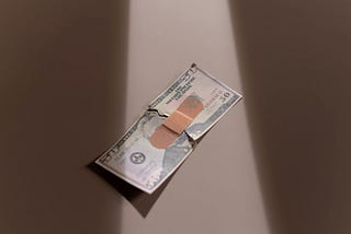 A U.S. fifty dollar bill is held together by a singular flexible fabric bandage.